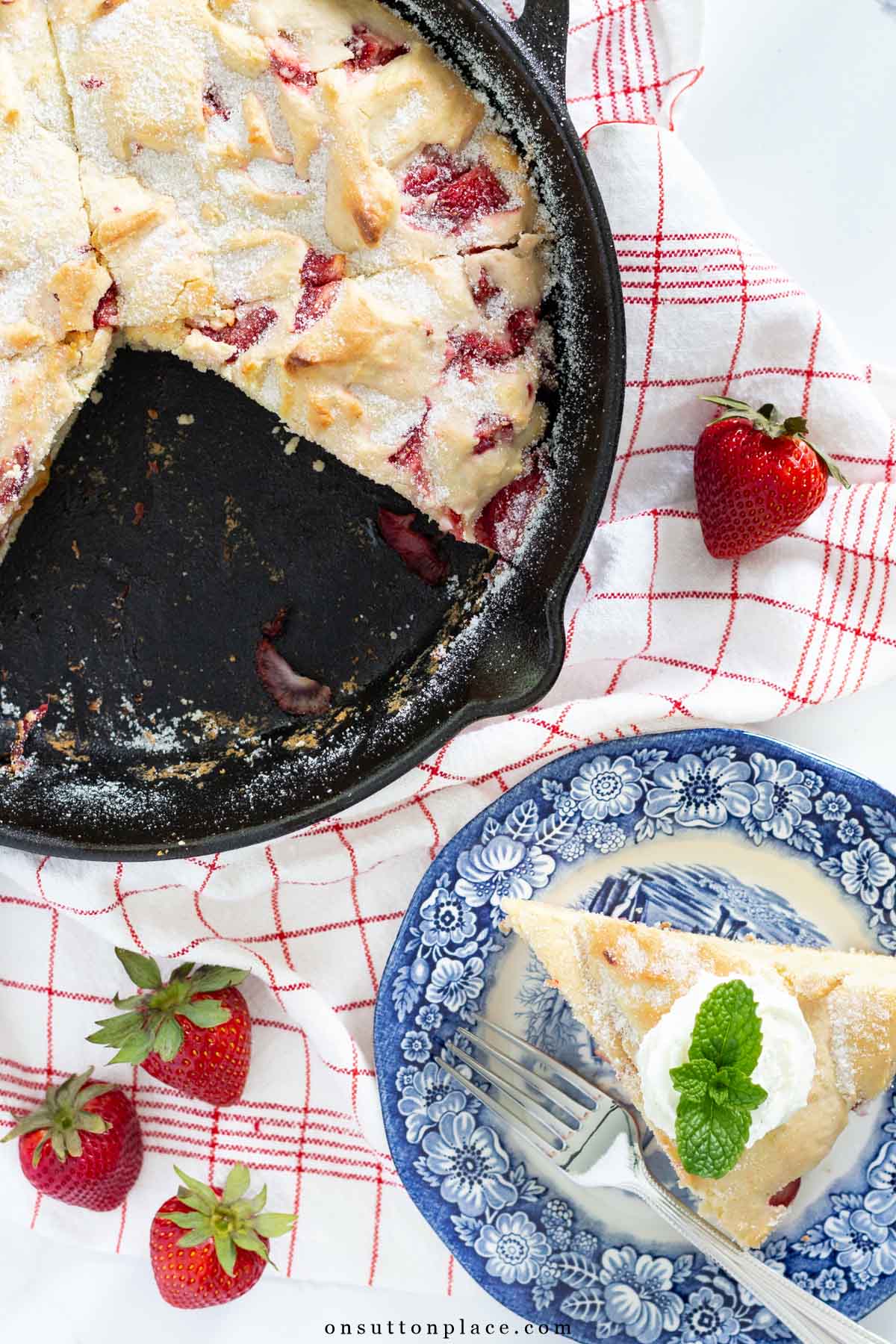 piece of strawberry cake on blue plate with cast iron skillet