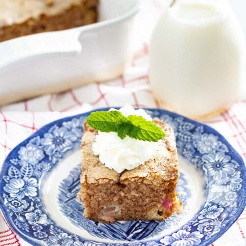 piece of rhubarb cake on blue plate with whipped cream and mint garnish