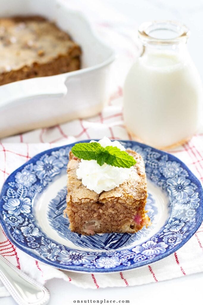 piece of rhubarb cake on blue plate with whipped cream and mint garnish