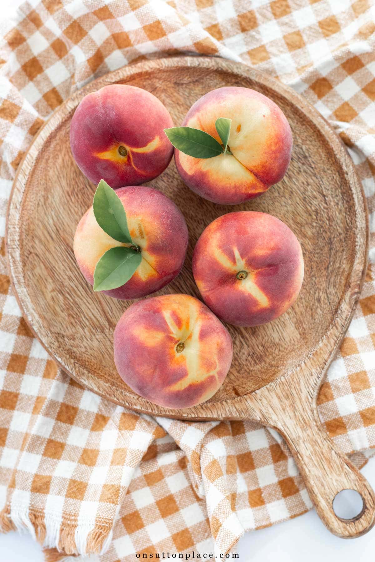 fresh peaches on round wood board on gingham towel