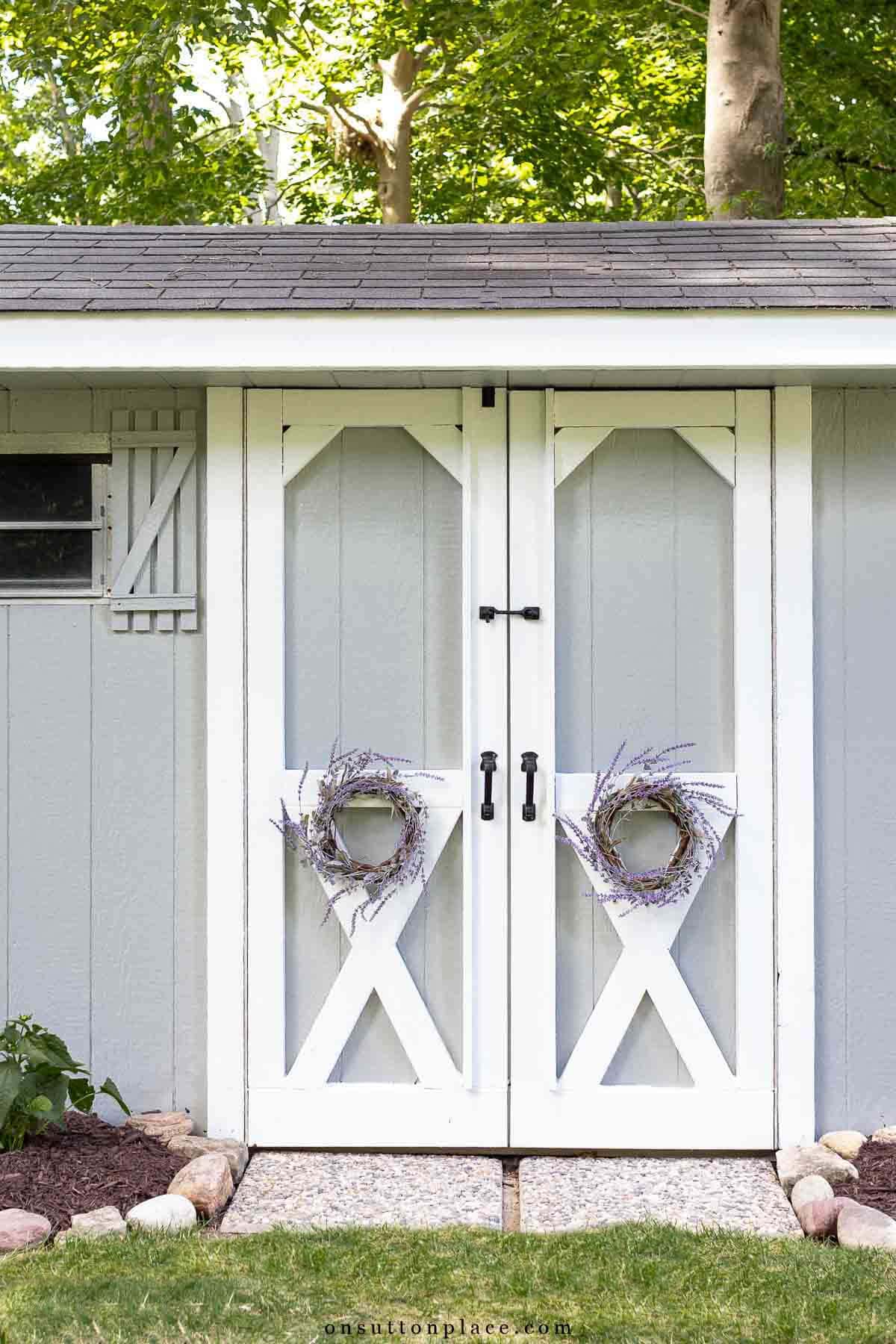 outdoor storage shed makeover ideas gray white paint wreaths on doors pavers rock border (1)