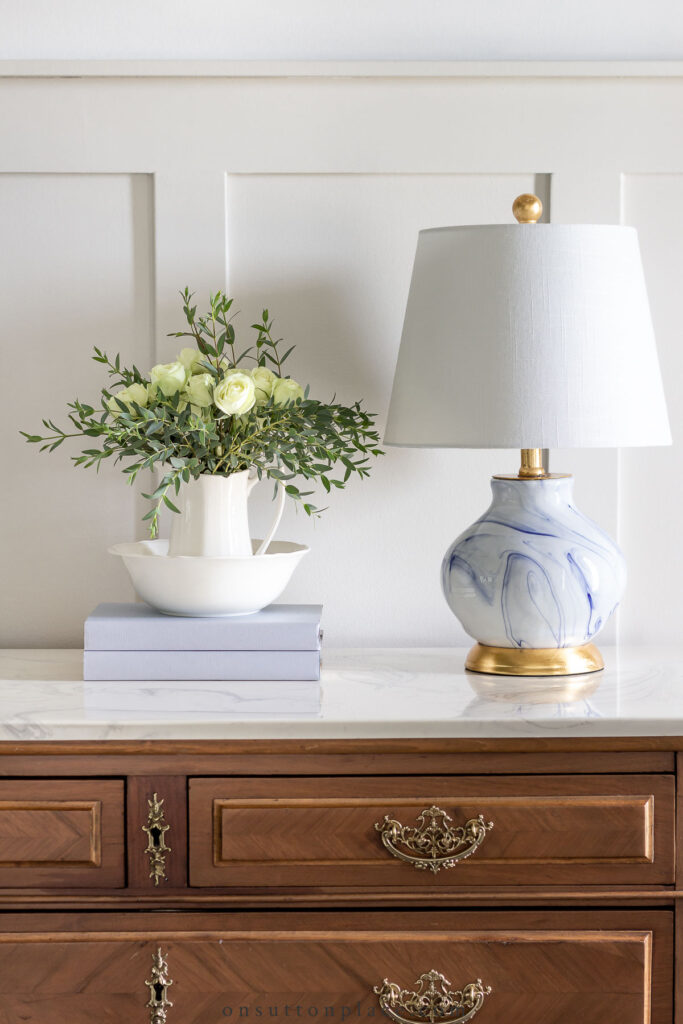 lamp books and flowers on marble top dresser