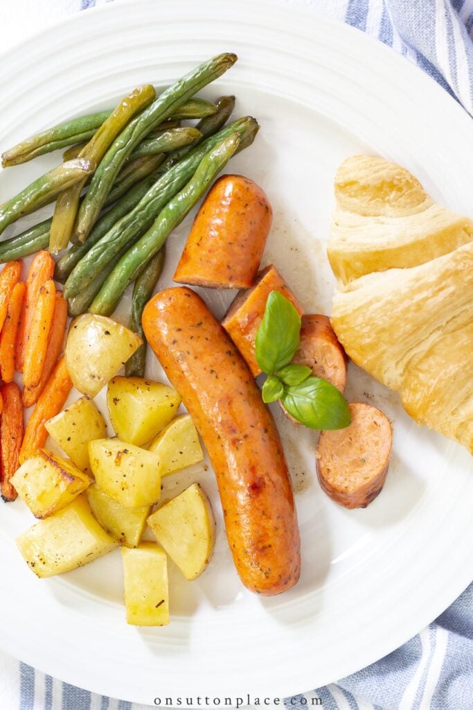 chicken sausage potatoes carrots green beans croissant on plate
