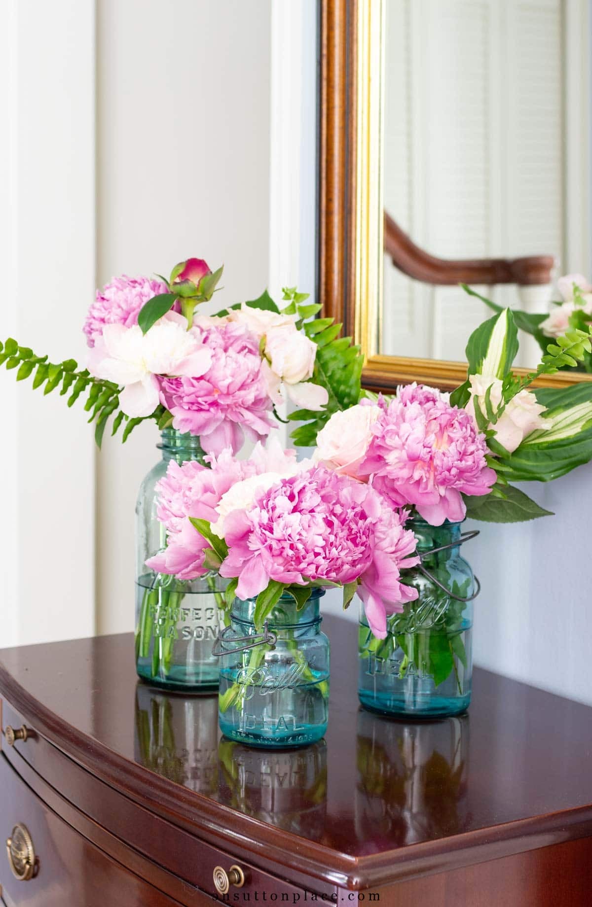 peonies and hosta leaves in blue mason jars on small chest