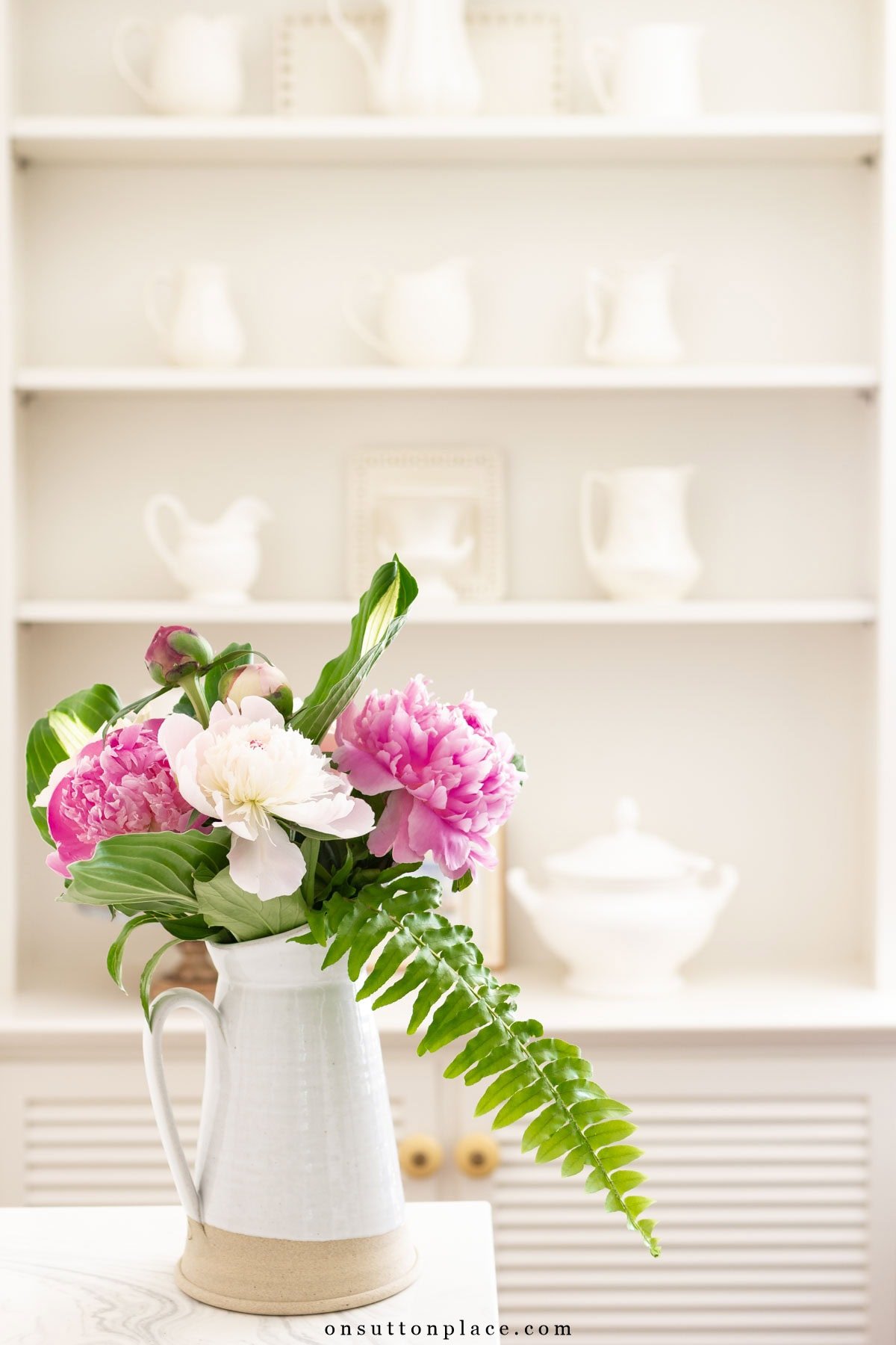 peonies fern fronds hosta arranged in farmhouse pitcher