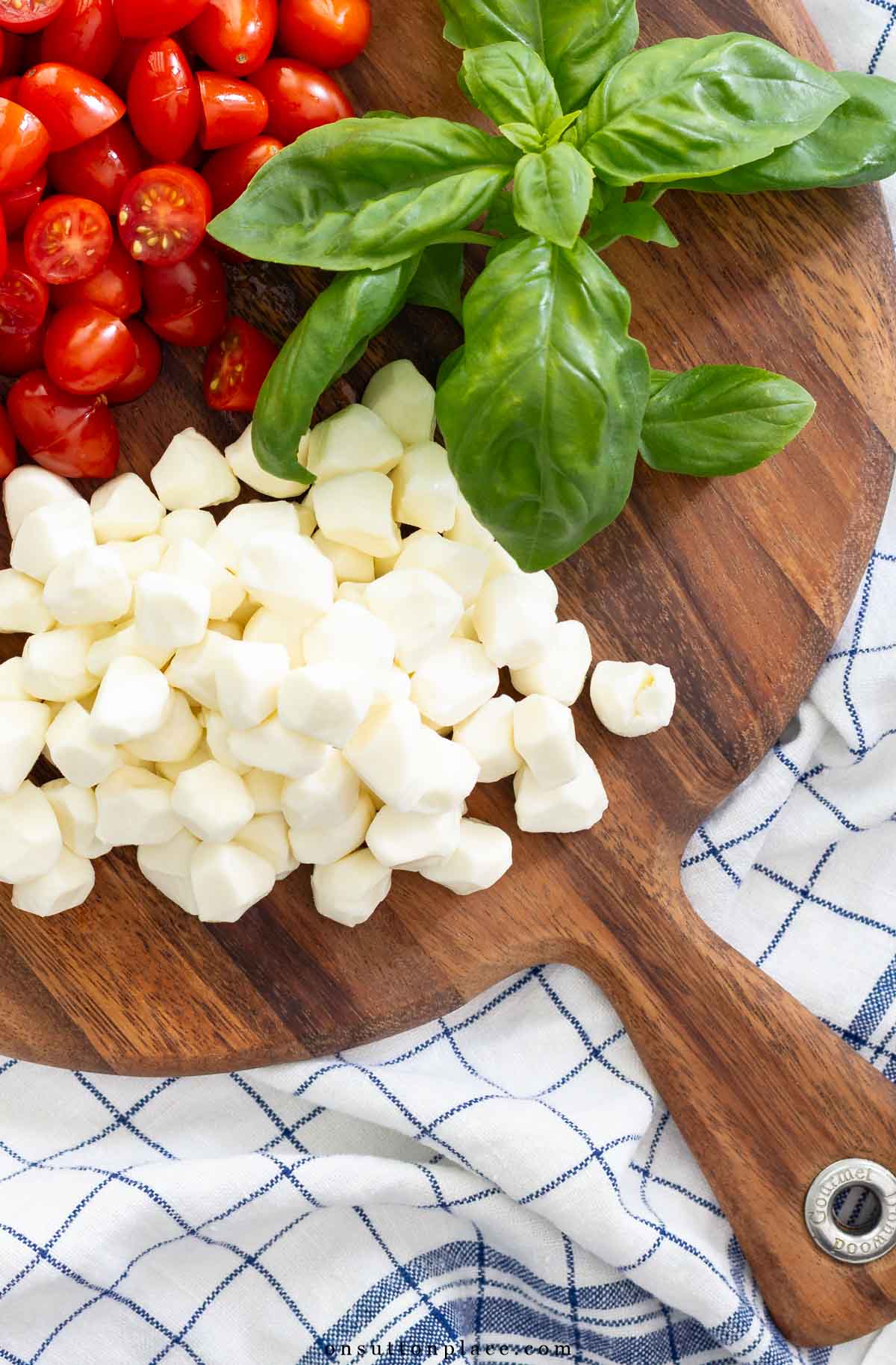 ingredients for caprese salad on round wood board blue plaid towel