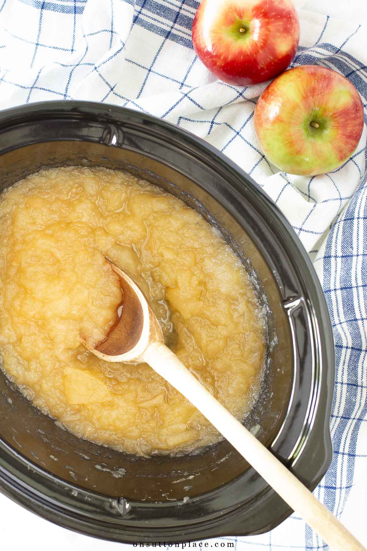 crockpot applesauce with wooden spoon apples on the side blue and white towels