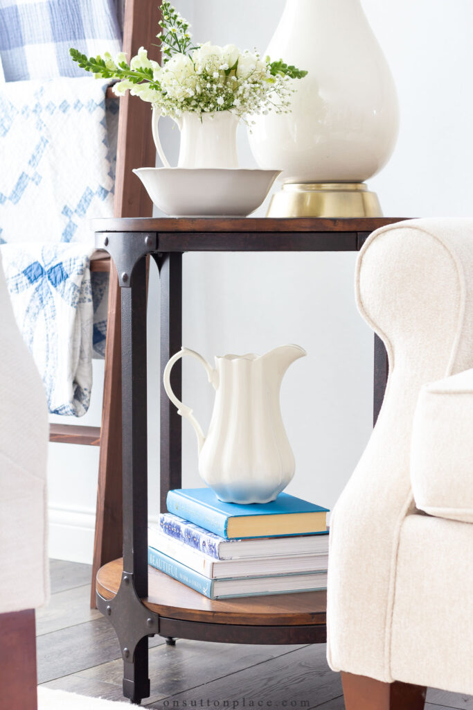 stack of books with pitcher on bottom shelf of end table tips for a simpler life