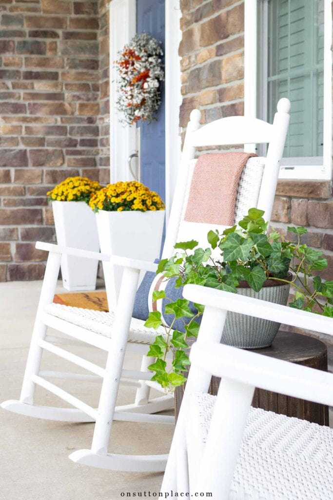 white porch rocker with throw blanket blue front door white planters with mums-15