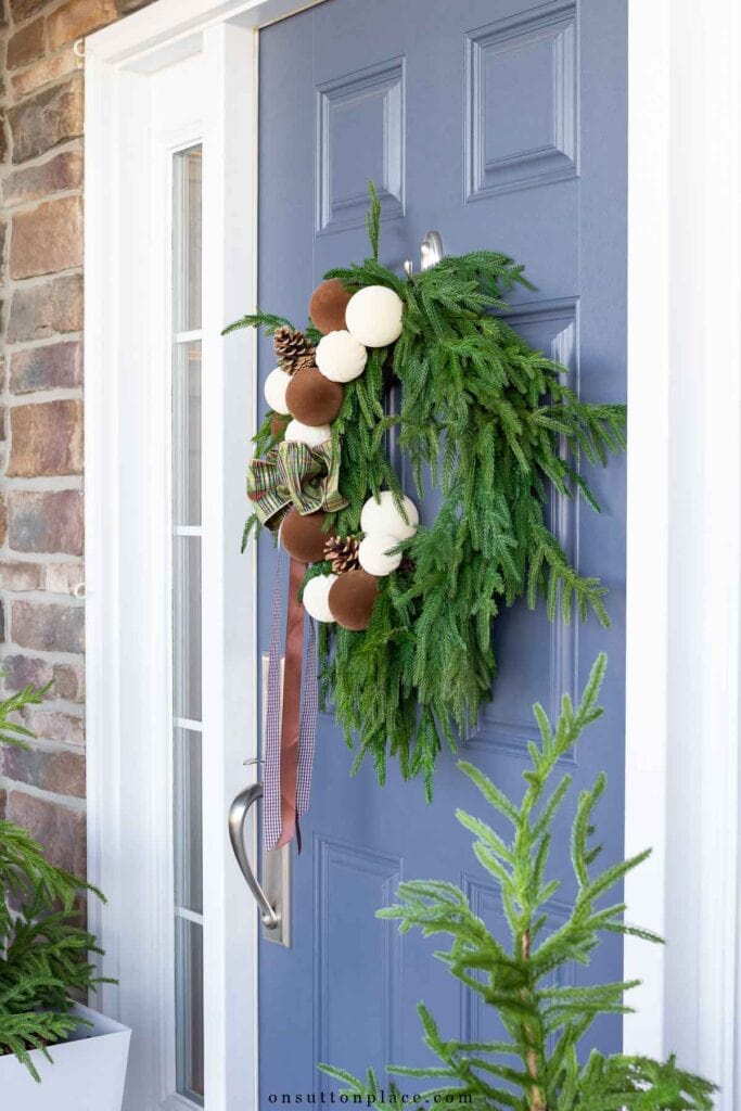 Norfolk pine wreath with neutral ornaments on blue front door