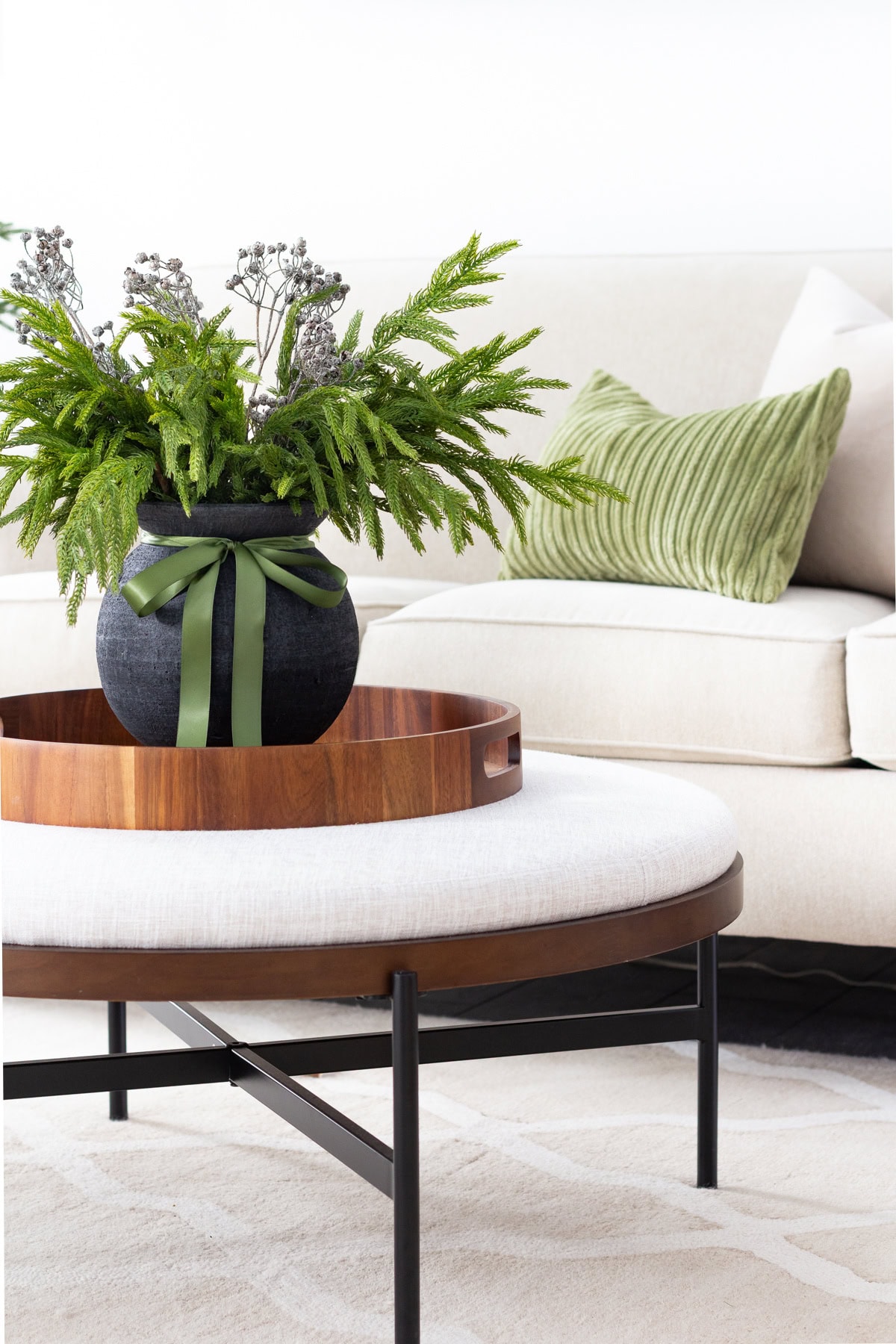 upholstered coffee table with wood tray and evergreen arrangement