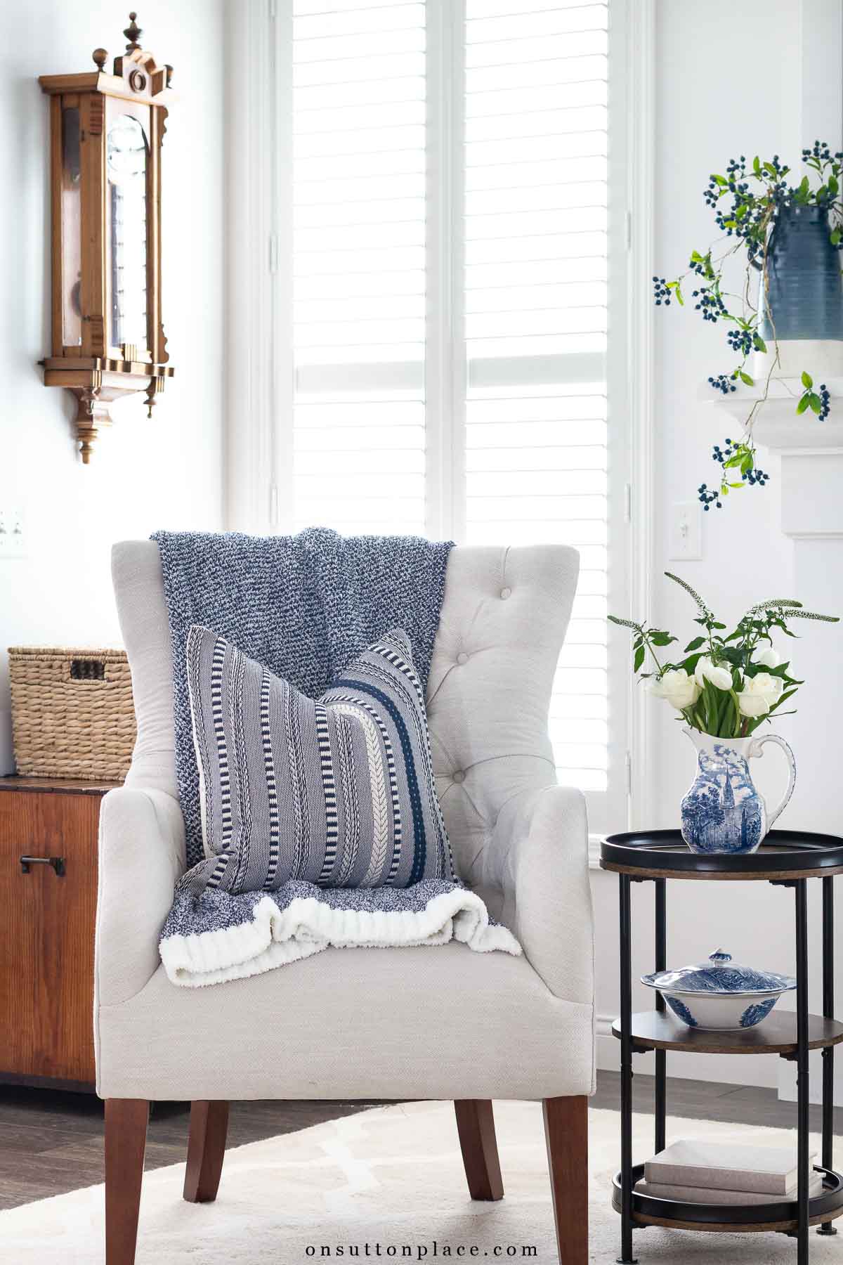 corner of neutral living room with tufted chair round table clock on wall