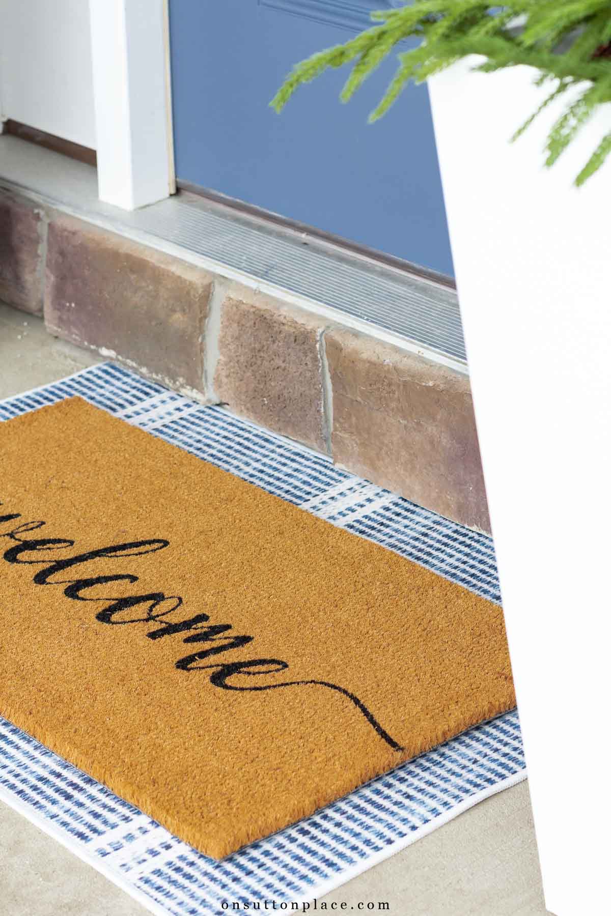 welcome mat layered over blue striped run in fron of door
