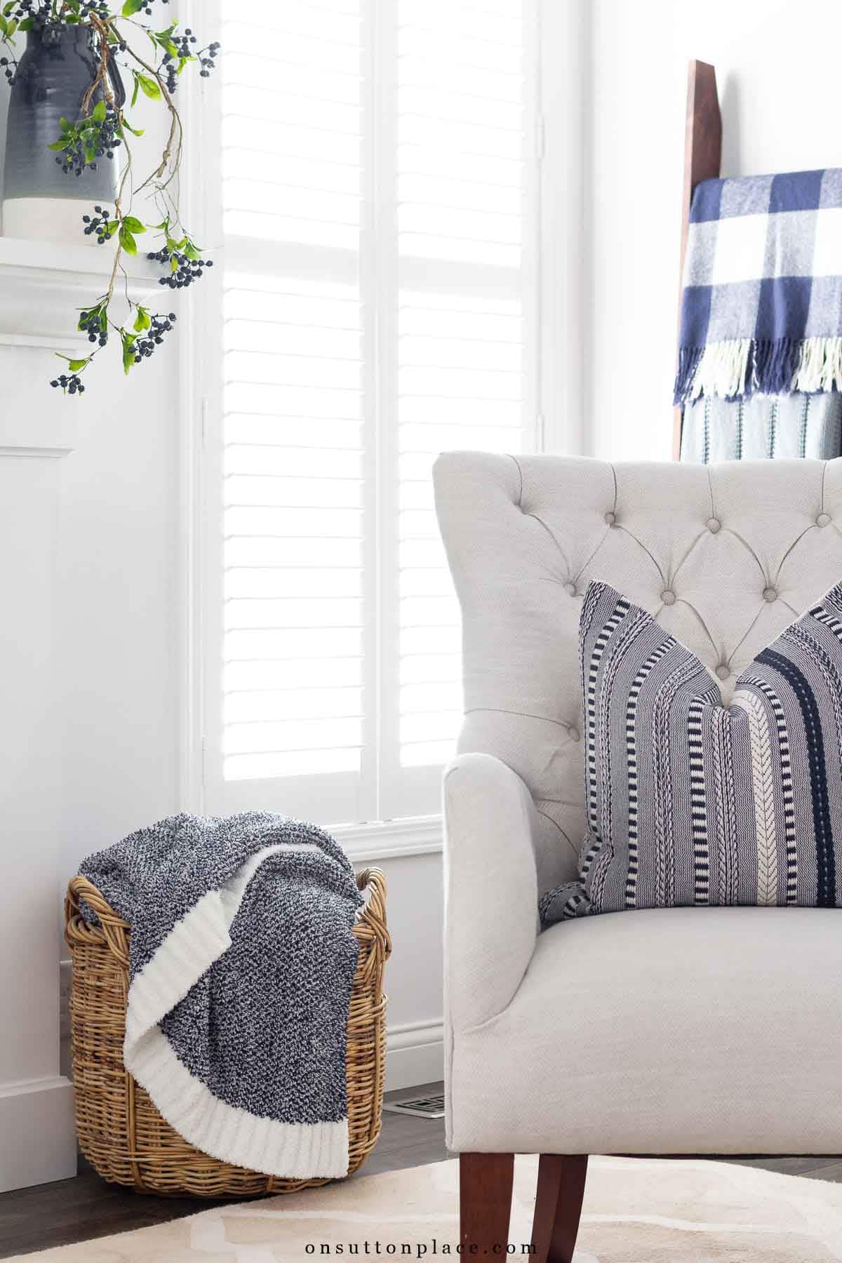 a well kept home with a basket of throw blankets beside tufted chair