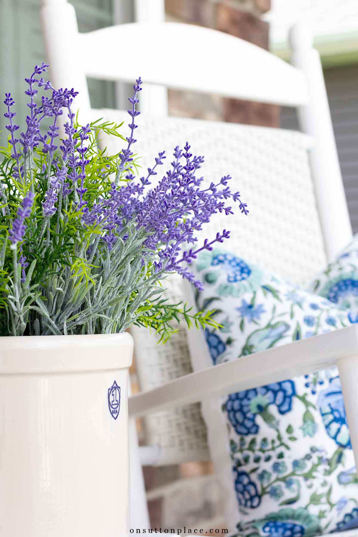 front porch flower pot with faux lavender beside white rocker