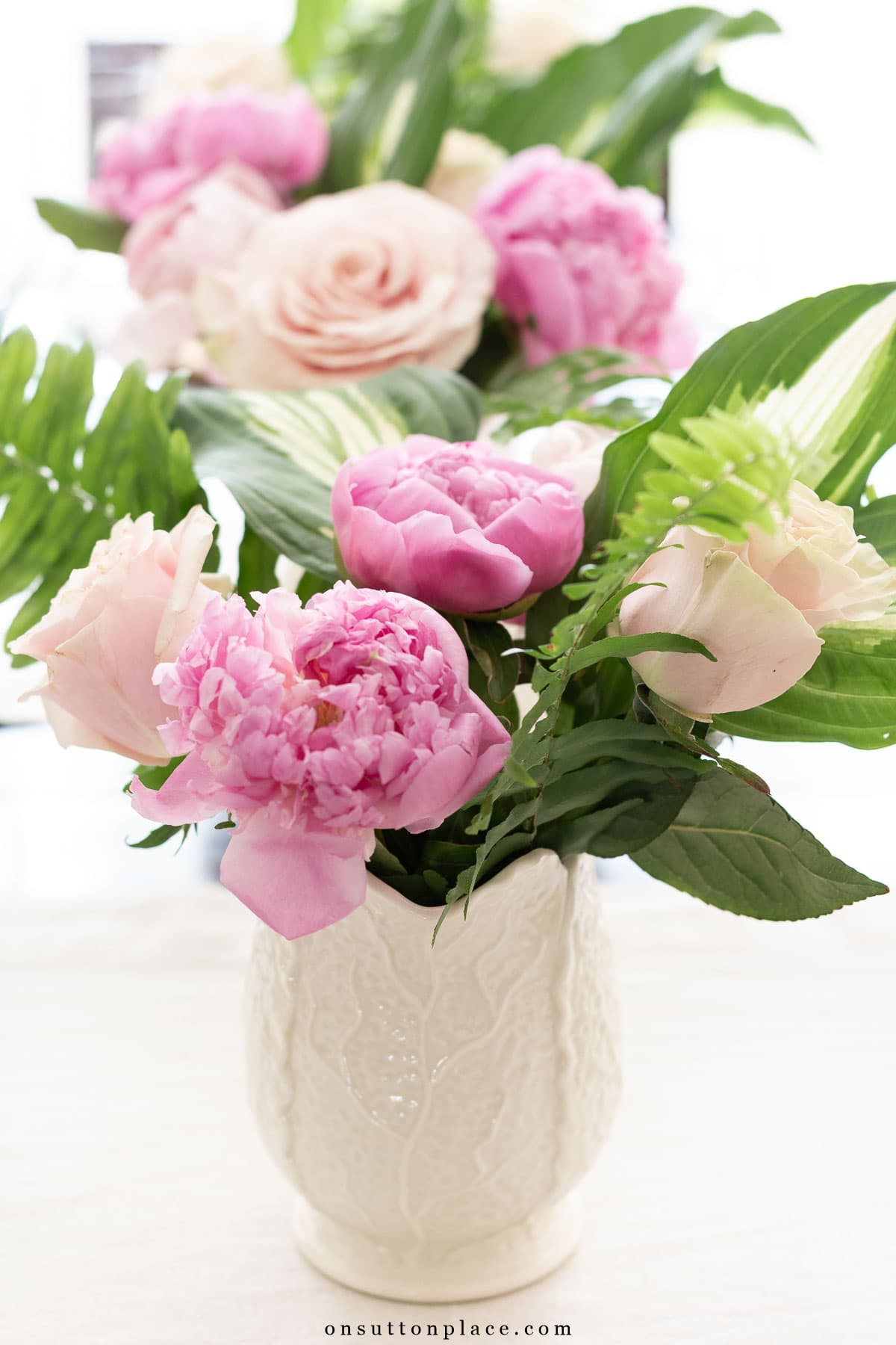 pitcher of pink peonies with hosta leaves and fern fronds