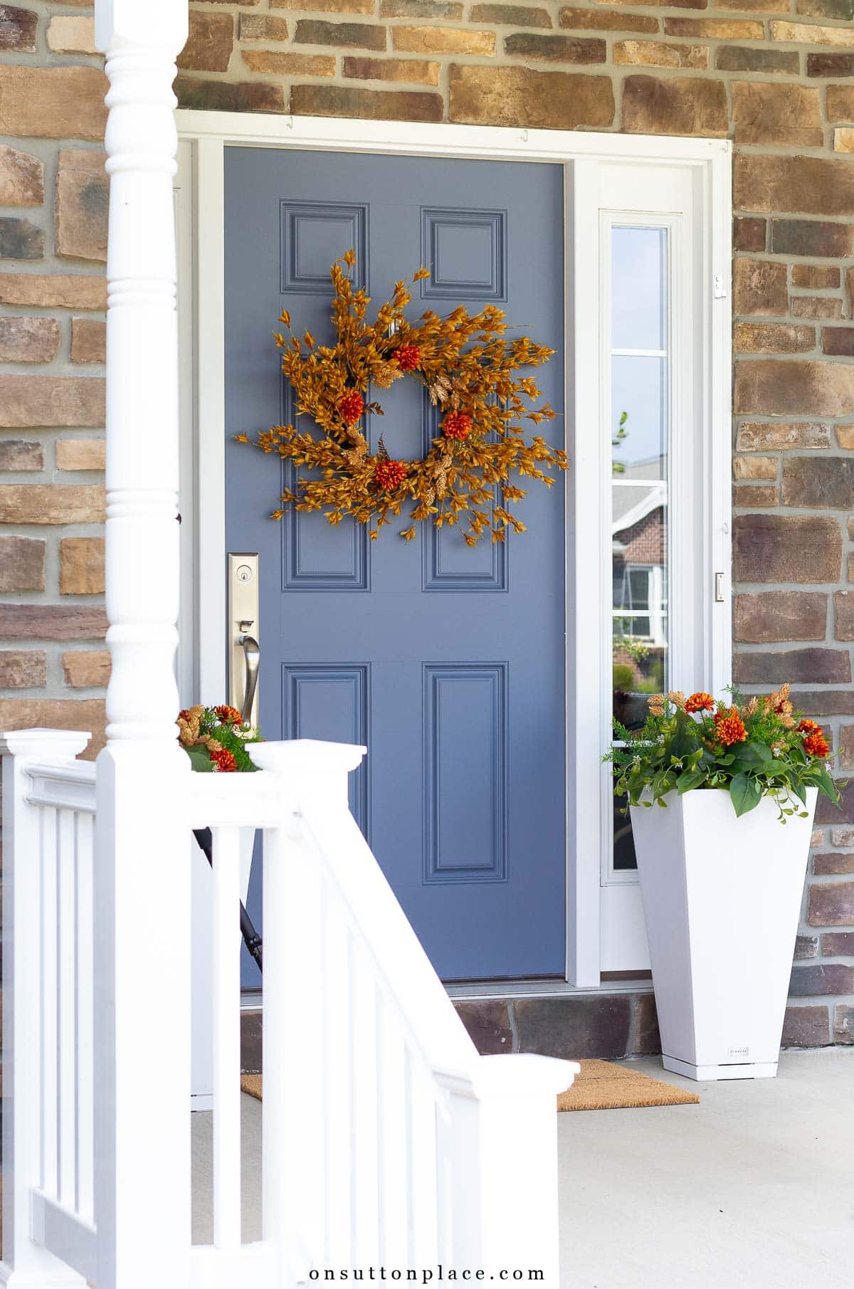 blue front door on porch with fall wreath and planters