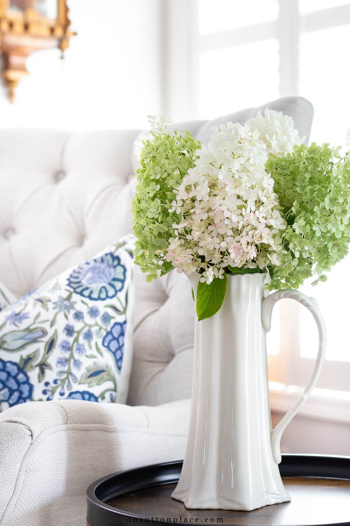 limelight hydrangeas in pitcher beside tufted chair